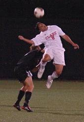 A Clark University player winning a header duel against an opposing player during a match