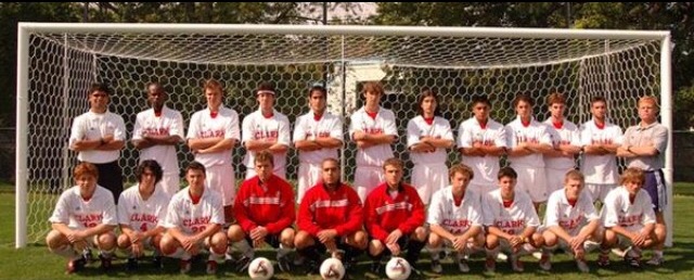 The Clark University men's soccer team posing in white and red kits in front of a goal on the field
