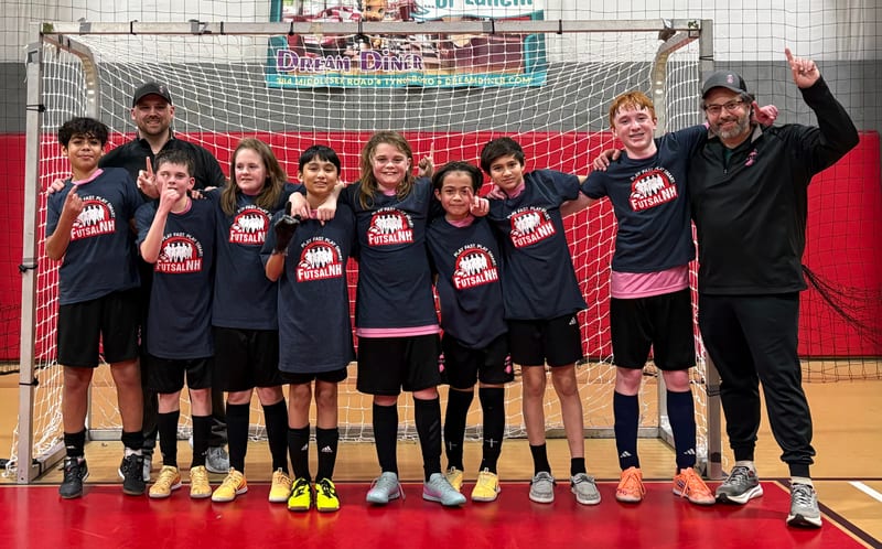 A boys team in navy FutsalNH shirts posing with two coaches in front of a futsal goal