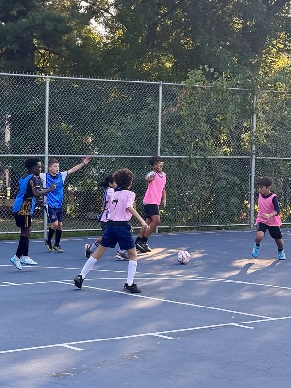 A group of players in pink and blue pinnies reacting to play on an outdoor court