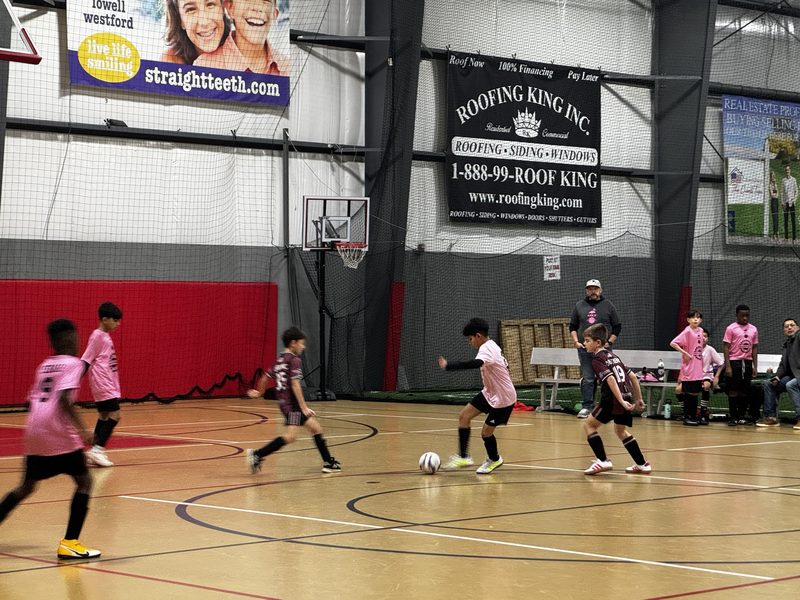 Players in pink and maroon jerseys challenging for the ball on an indoor futsal court