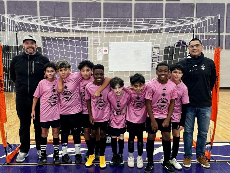 A boys team in pink Bob's Automotive jerseys posing with two coaches in front of a futsal goal